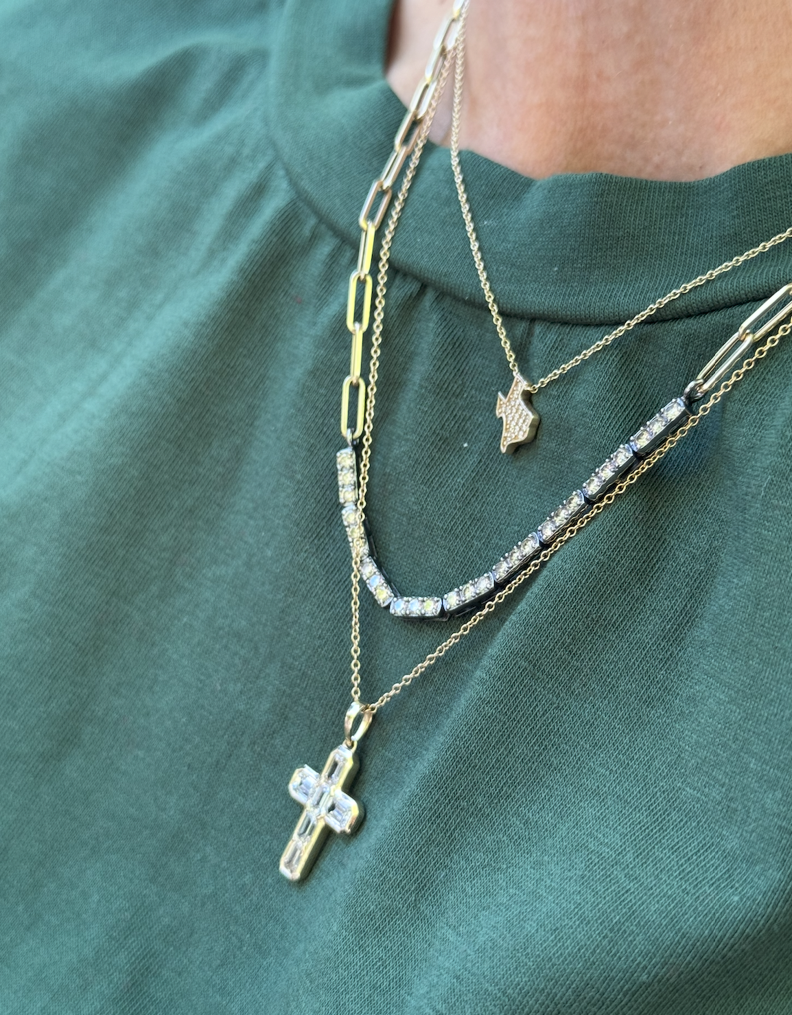 Close-up of layered gold necklaces with pendants on a green shirt.