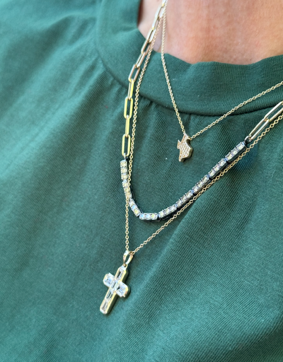 Close-up of layered gold necklaces with pendants on a green shirt.