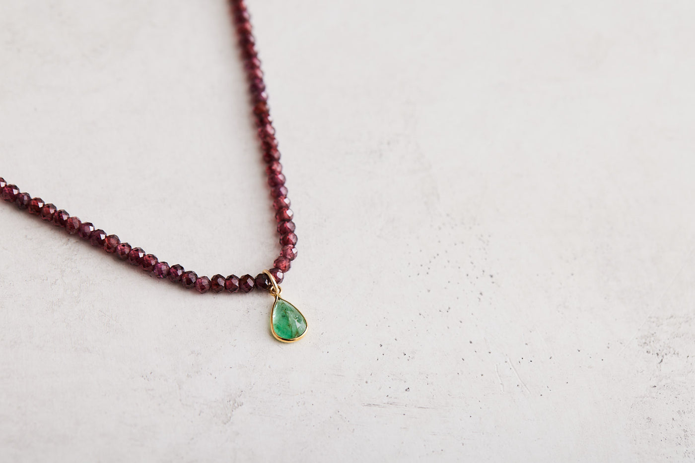 16" Faceted garnet necklace with a large natural teardrop emerald set in 14k yellow gold and finished with a 14k gold magnetic clasp. Handmade by Nicole Gerulat.